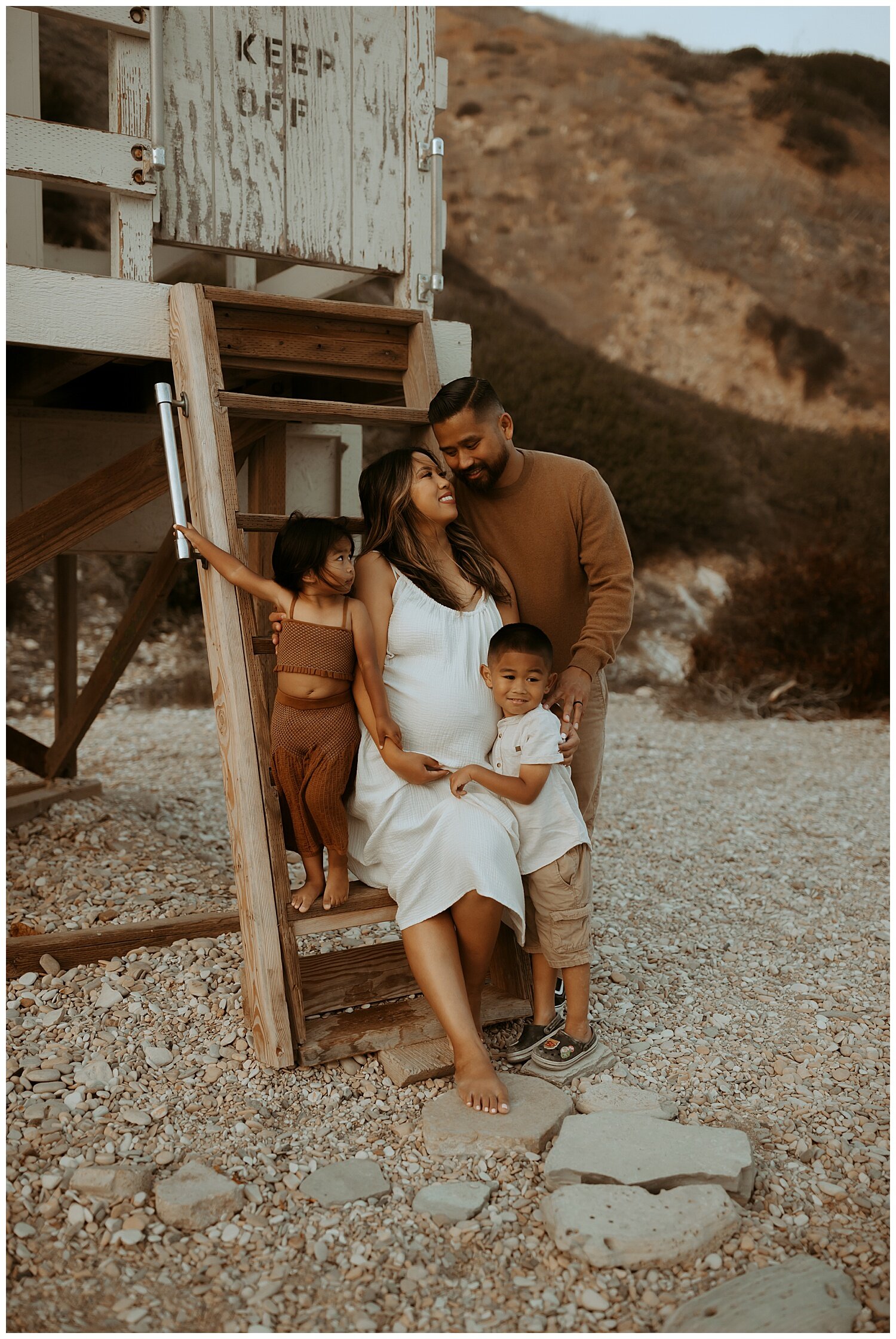 family on lifeguard stand on lots Angeles beach during three maternity photo shoot